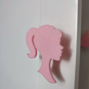 Peut inclure: Silhouette rose d'un profil féminin avec une queue de cheval. La silhouette est faite d'un matériau texturé et se détache sur un fond blanc. L'image est une prise de vue en gros plan.