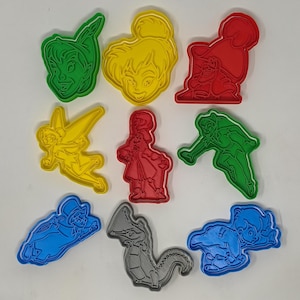 Puede incluir: Una colección de cortadores de galletas de plástico de colores en varias formas, incluyendo personajes de Peter Pan. Los cortadores son en tonos de verde, amarillo, rojo, azul y gris. Las formas incluyen Campanilla, Peter Pan y un cocodrilo.