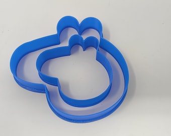 May include: A blue plastic cookie cutter shaped like a cartoon pig. The cutter has two layers, one slightly larger than the other.