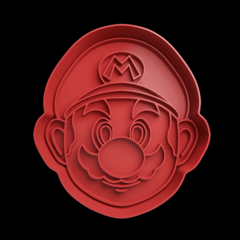 Puede incluir: Cortador de galletas de pl&aacute;stico rojo con forma de personaje de dibujos animados con bigote y sombrero. El personaje tiene una gran 'M' en la parte delantera del sombrero.