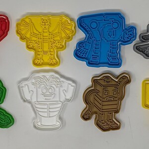 Könnte beinhalten: Eine Sammlung farbenfroher Ausstecher aus Kunststoff in verschiedenen Formen, darunter ein Roboter, ein Drache, ein Flugzeug und eine Teekanne. Die Ausstecher sind rot, gelb, blau, grau, grün, weiß, braun und gelb.