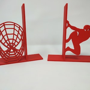 以下が含まれることがあります： スパイダーマンのシルエットとマスクが描かれた赤いブックエンドのペア。ブックエンドは丈夫な素材で作られており、本やその他のアイテムを置くのに最適です。