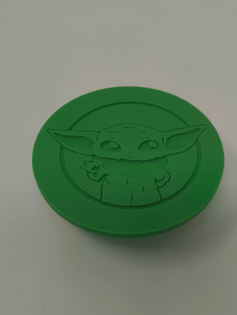 May include: A green, circular object featuring a raised relief of a character with large ears and wide eyes. The character is centered within a circular border. The object is a solid, vibrant green color.