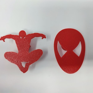May include: Two red 3D printed figures of a superhero. One figure is a silhouette of a superhero in a crouching pose with arms outstretched. The other figure is a silhouette of a superhero mask with a spider web design.