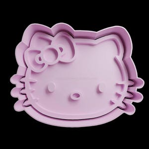 May include: A light purple plastic cookie cutter shaped like Hello Kitty. The cutter has a bow on top of her head and a small nose.