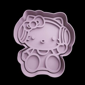 May include: Purple plastic cookie cutter shaped like a cartoon cat wearing headphones. The cat has a bow on its head and a big smile.