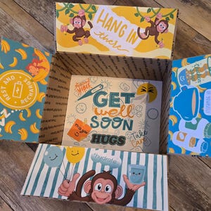 May include: A get well soon gift box with a blue and yellow banana pattern, a monkey graphic, and the text "Hang in there", "Get well soon", "Take care", "Hugs", and "Hydrate".