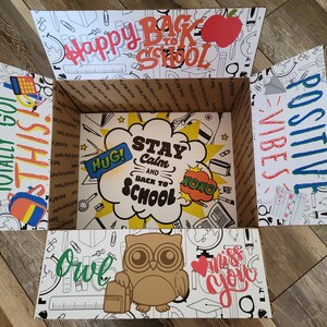 Könnte beinhalten: Ein weißer Karton mit einem bunten Back-to-School-Motiv. Die Box ist geöffnet und das Innere ist sichtbar. Die Box ist mit Zeichnungen von Schulutensilien, einer Eule und den Worten "You've Totally Got This", "Happy Back to School", "Stay Calm and Back to School", "Positive Vibes" und "Owl" verziert.