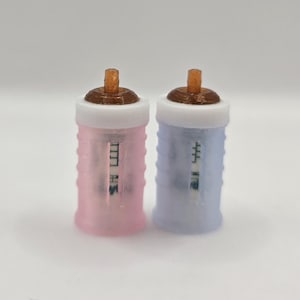May include: Two cylindrical fuel filters with translucent pink and light blue bodies. Each filter features a white top cap, a small brown nozzle, and a visible internal paper element. The design includes a ribbed exterior texture for grip.