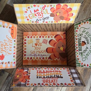 Könnte beinhalten: Ein Karton, der mit Thanksgiving-Motiven bedruckt ist. Der Karton ist geöffnet und enthält mehrere bunte Karten mit Botschaften wie "Ich bin so dankbar für dich" und "Ich liebe dich so sehr, ich vermisse dich".