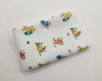 Pode incluir: Uma peça de tecido retangular branca dobrada com um padrão repetitivo de pequenos pintinhos coloridos de desenho animado em amarelo, laranja e azul, intercalados com pequenos detalhes florais verdes e azuis na superfície do material.