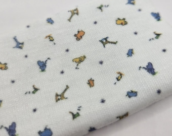 Pode incluir: Um tecido branco com um padrão repetitivo de pequenas ilustrações coloridas de vários animais e figuras, incluindo formas azuis, amarelas e laranjas, intercaladas com minúsculos pontos azul-escuros em toda a superfície do material.