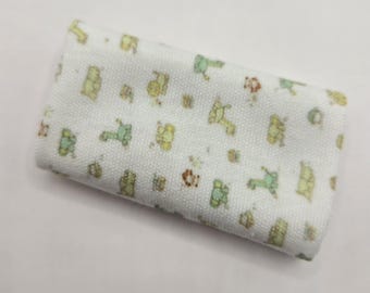 Pode incluir: Uma peça de tecido retangular branca com uma superfície texturizada, apresentando um padrão repetitivo de pequenas ilustrações de animais em verde claro e amarelo, incluindo girafas e elefantes, distribuídas uniformemente por toda a superfície.
