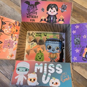 Op de afbeelding: Een Halloween-thema cadeaudoos met verschillende decoraties, waaronder een monster, een vampier en een mummie. De doos is versierd met de woorden "Just a little batty without you" en "Miss you".