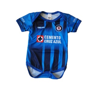 May include: Blue and black baby bodysuit with the text "CRUZ AZUL" and a team logo. The bodysuit has a round neck and short sleeves. The front features vertical stripes and the words "CEMENTO CRUZ AZUL".