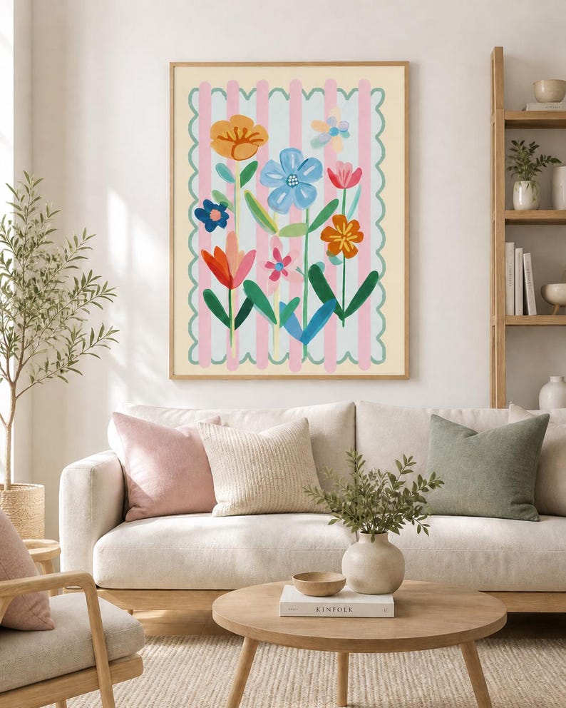 May include: A framed floral art print with vibrant flowers set against a pink and white striped backdrop. The artwork hangs above a cream sofa with cushions. A wooden coffee table, holding a vase and a book, sits in front of the sofa.