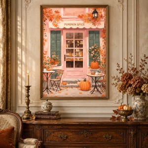 Peut inclure: Une impression d'art encadrée représentant une devanture de magasin rose avec le texte PUMPKIN SPICE au-dessus de la porte. La scène présente un feuillage d'automne, des citrouilles orange, deux petites tables de bistrot et une lanterne.
