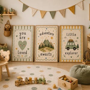 Op de afbeelding: Drie ingelijste wandposters met illustraties van een hart met de tekst you are loved, een berglandschap met de tekst adventure awaits, en een auto met de tekst little explorer, tentoongesteld in een kamer met kinderkamerdecoratie.