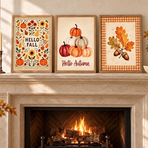 May include: Three framed wall art prints featuring seasonal motifs. The left print displays flowers, leaves, and pumpkins with the text "HELLO FALL". The center print shows a stack of pumpkins with the text "Hello Autumn". The right print shows oak leaves and acorns.