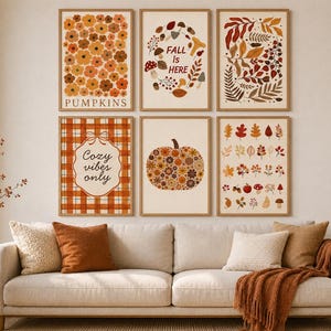 May include: A set of six framed wall art prints featuring autumn themes. The prints display orange and brown flowers, mushrooms with the text FALL IS HERE, foliage, a plaid pattern with the text Cozy vibes only, a floral pumpkin, and various leaves.