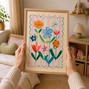 May include: A framed floral art print featuring colourful flowers on a cream background with pink stripes. The artwork includes orange, blue, and red flowers with green stems and leaves, set within a light brown wooden frame.
