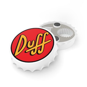May include: White bottle opener with a red and yellow Duff logo on the top. The bottle opener is shaped like a bottle cap.