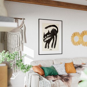 May include: A white sofa with a black and white throw blanket, green and brown cushions, and a framed black and white illustration of a cat. The illustration is titled "CAT". There are three straw sunburst mirrors on the wall behind the sofa.