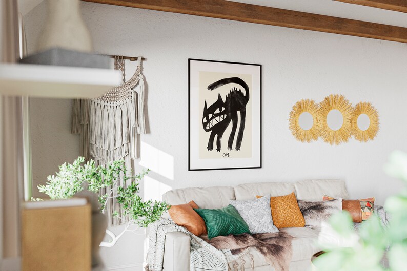 May include: A white sofa with a black and white throw blanket, green and brown cushions, and a framed black and white illustration of a cat. The illustration is titled "CAT". There are three straw sunburst mirrors on the wall behind the sofa.