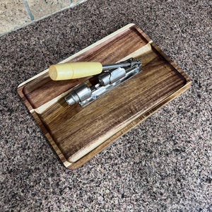 May include: A rectangular wooden serving tray with a light-colored handle corkscrew and a stainless steel corkscrew. The tray has a dark brown border and a lighter brown interior. The handle is a light yellow color.