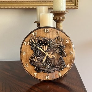 May include: A wooden clock with an American flag and eagle design. The clock face has Roman numerals and the hands are gold. The clock is on a wooden table.