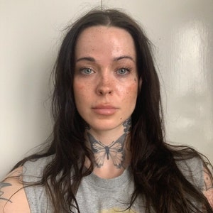 Könnte beinhalten: Eine Frau mit langen dunklen Haaren und einem Schmetterlingstattoo am Hals trägt ein graues ärmelloses Shirt.