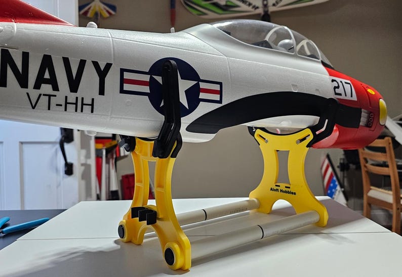 K&ouml;nnte beinhalten: Ein gelber und wei&szlig;er Flugzeugst&auml;nder mit einem wei&szlig;en Flugzeug darauf. Das Flugzeug ist mit den Worten "NAVY VT-HH" und der Nummer "217" bemalt.