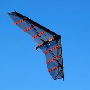Puede incluir: Un avión teledirigido negro y naranja con una envergadura de aproximadamente 90 cm. El avión está volando en un cielo azul claro.