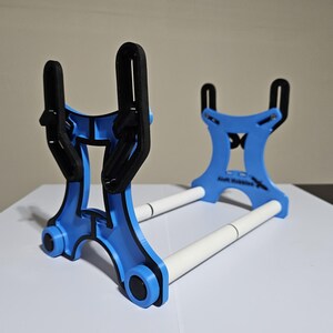 K&ouml;nnte beinhalten: Ein blauer und schwarzer 3D-gedruckter St&auml;nder mit zwei wei&szlig;en Stangen. Der St&auml;nder ist so konzipiert, dass er zwei Gegenst&auml;nde, wie z. B. Telefone oder Tablets, aufnehmen kann.