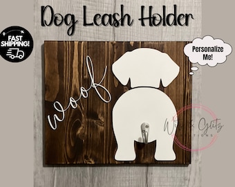 May include: Wooden dog leash holder with a white silhouette of a dog's rear end and the word "woof" written in white script. The holder has a metal hook for hanging leashes. The text "Personalize Me!" is written in a thought bubble.