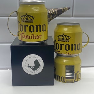 May include: A set of two yellow Corona beer can candles. The candles are hand-poured and have a  "LifeScent by Celest Candles" label. The larger candle is shaped like a teapot with a brown paper spout.