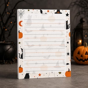 May include: A rectangular notepad featuring a white background with a border of Halloween icons including orange pumpkins, black cats, witch hats, ghosts, spiders, webs, and stars. The center contains horizontal lines for writing notes.