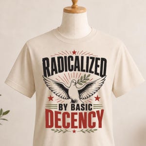 May include: Cream-coloured t-shirt featuring the text "RADICALIZED BY BASIC DECENCY" in a distressed font. A dove with outstretched wings and an olive branch is centered below the word "RADICALIZED". Red stars and lines complete the design.