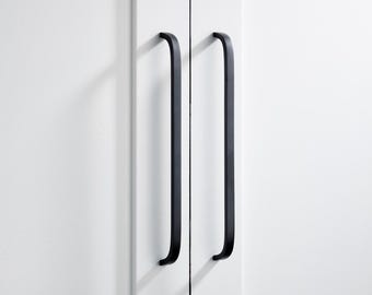 May include: Two black, curved cabinet pulls mounted on a white cabinet door. The pulls are long and slender, with a simple, modern design. The cabinet door is clean and minimalist, with a smooth, white surface. The pulls are evenly spaced and add a touch of elegance.