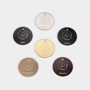 May include: Six circular metal tags with a single hole at the top. Each tag features the Pushka Home logo and text, with labels for silver, grey, black, gold, antique gold, and bronze finishes, showcasing distinct metallic colors and textures.