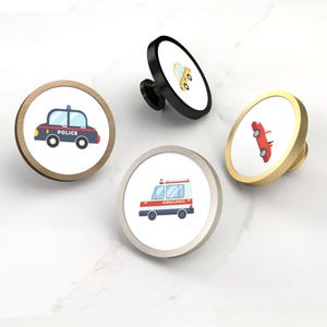 Pode incluir: Conjunto de quatro puxadores decorativos para armários com desenhos de veículos. Inclui um carro de polícia, uma ambulância, um táxi e um carro vermelho. Cada puxador tem um acabamento metálico diferente: dourado, preto, prateado e latão. Os puxadores são redondos.