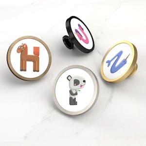 May include: Four decorative cabinet knobs with animal and letter designs. The knobs feature a brown horse with the letter "H", a pink unicorn with the letter "U", a panda bear, and a blue narwhal with the letter "N". The knobs have gold, silver, and black finishes.