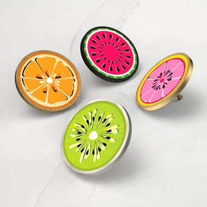 May include: Four cabinet knobs with fruit slice designs: an orange, a watermelon, a pink grapefruit, and a kiwi. Each knob features a different fruit design with bright colours and a metallic finish. These knobs are perfect for adding a touch of fun to any furniture.