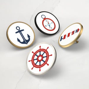 Peut inclure: Quatre boutons de meuble sur le thème nautique avec des fonds blancs et des bords dorés, argentés et noirs. Les motifs comprennent une ancre marine, une boussole rouge et noire, un phare rayé rouge et blanc et un gouvernail rouge et marine.