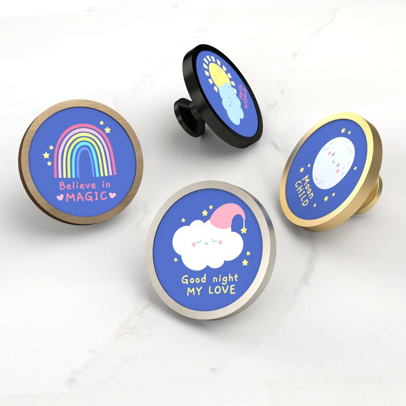 K&ouml;nnte beinhalten: Vier dekorative Schrankkn&ouml;pfe mit blauen Hintergr&uuml;nden und verschiedenen Designs. Ein Knopf zeigt einen Regenbogen und den Text "Believe in MAGIC". Ein anderer hat eine Sonne und Wolken. Ein dritter hat eine Wolke mit Nachtm&uuml;tze und dem Text "Good night MY LOVE". Der letzte Knopf hat einen Mond und den Text "Moon CHILD".