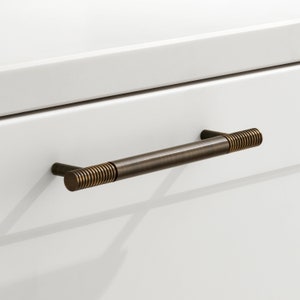 Könnte beinhalten: Ein gebürsteter Bronze-Schrankgriff mit einem strukturierten, gerippten Design. Der Griff ist etwa 12,7 cm lang.