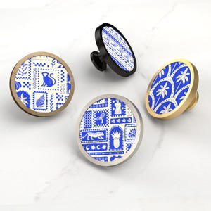 May include: Four decorative cabinet knobs with blue and white patterns. The knobs have different shapes and finishes, including round and oval designs. One knob has a black base, while another has a gold finish. The patterns include botanical and animal motifs.