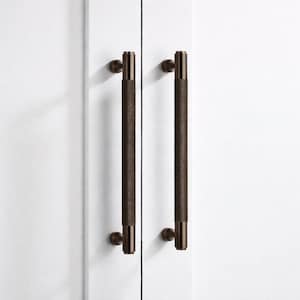 Puede incluir: Dos tiradores de armario de color bronce con un agarre cilíndrico texturizado. Los tiradores están montados en una puerta de armario blanca. El herraje tiene un diseño moderno y minimalista.