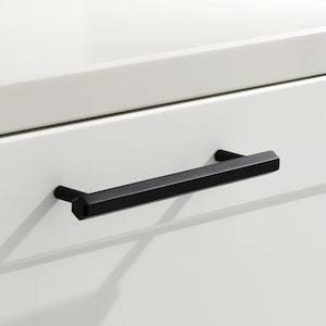 May include: Black cabinet drawer pull with a rectangular shape and slightly angled edges.