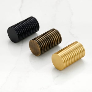 Può includere: Tre pomelli per armadi con un design a coste. I pomelli sono in finiture nero, ottone e oro.